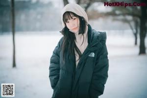 A woman standing in the snow wearing a black coat.