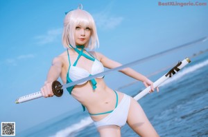 A woman in a bikini holding a sword on the beach.