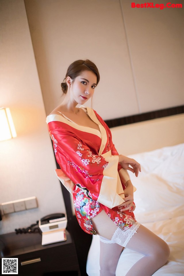 A woman in a red kimono sitting on a bed.