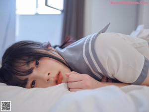 A woman in a school uniform is sitting on a bed.