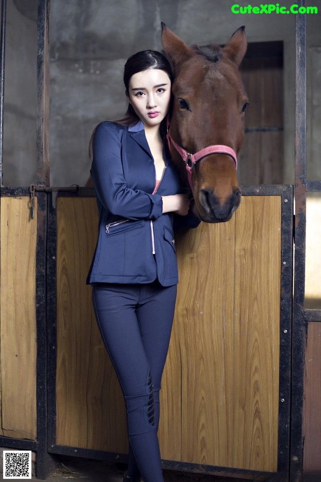 A woman standing next to a brown horse in a stable.