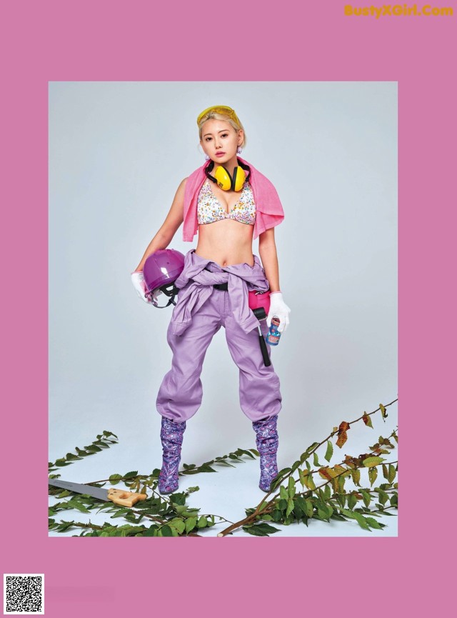 A woman in a pink top and purple pants holding a purple helmet.