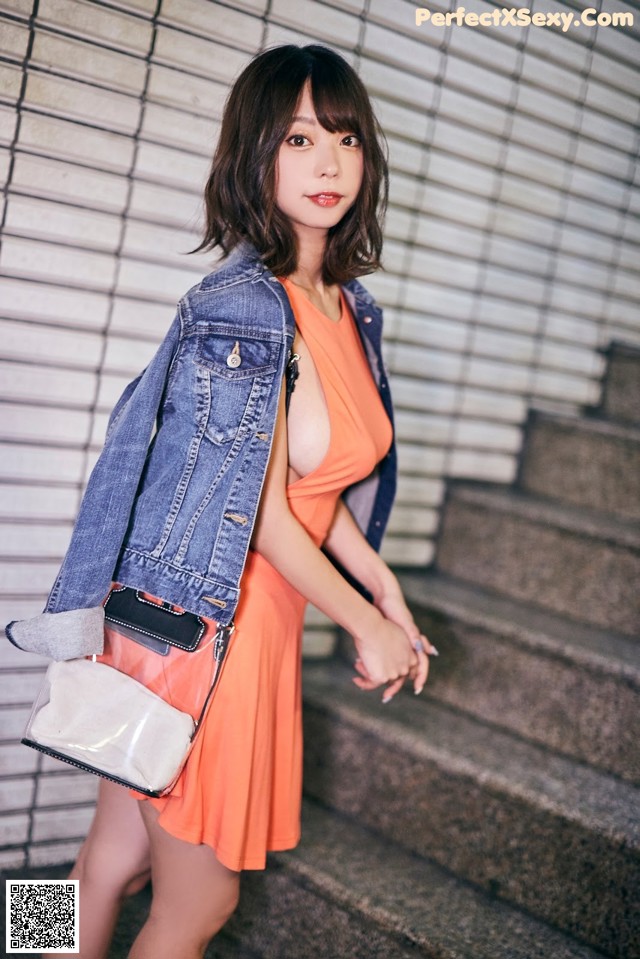 A woman in an orange dress and a denim jacket posing for a picture.