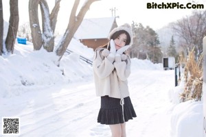 A woman in a white sweater and black skirt posing in the snow.