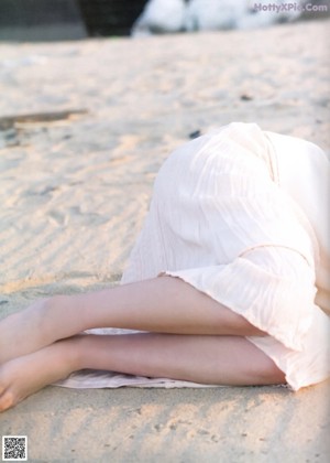 A woman laying on the sand with her head resting on her hands.