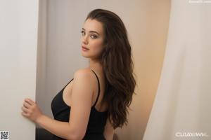 A naked woman with long brown hair sitting on a bed.