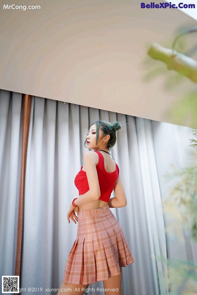 A woman in a red top and plaid skirt posing for a picture.