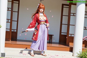 A woman in traditional attire holds a sword, standing near a wooden post and large stones.