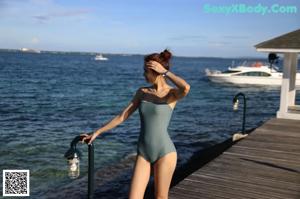 A woman in a green one piece swimsuit standing by a pool.