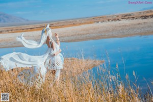 A woman in a white dress standing in a field of tall grass.