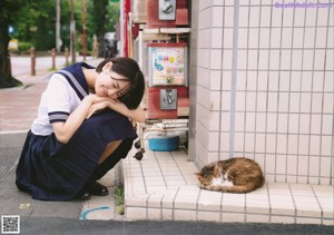 A woman in a school uniform leaning against a fence.