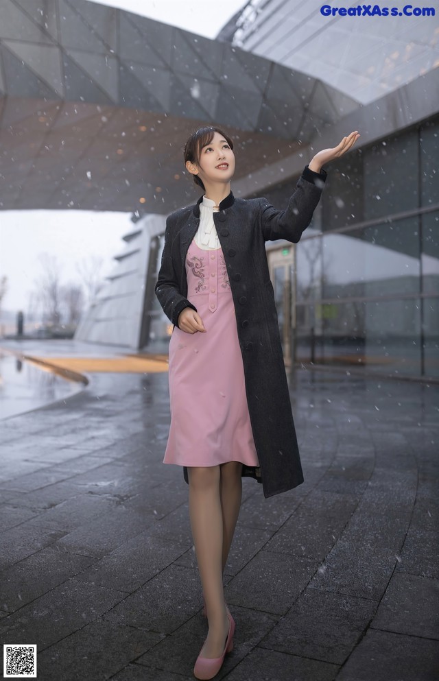 A woman in a pink dress and black coat standing in the rain.