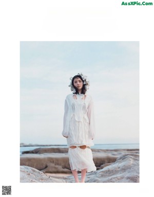 A woman in a white dress standing on top of a hill.