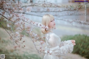 A woman in a white dress standing in front of a tree.