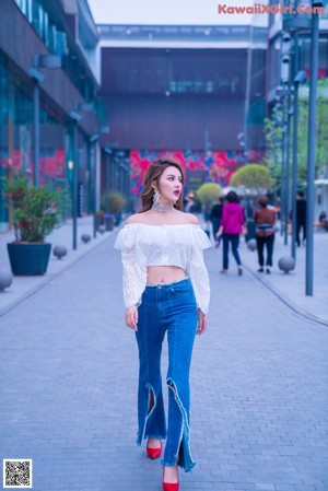 A woman standing in front of a wall wearing a white top and jeans.