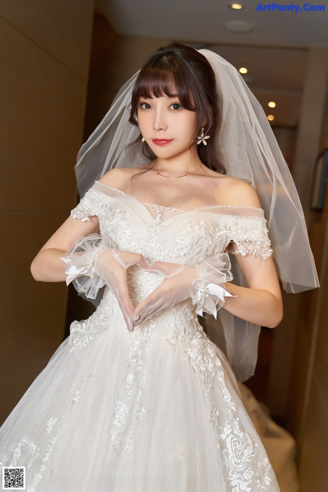 A woman in a wedding dress making a heart with her hands.