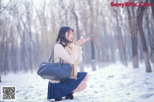 A woman sitting in the snow with a handbag.