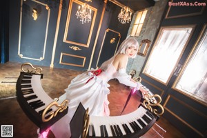 A woman in a white and pink dress sitting on a white piano.